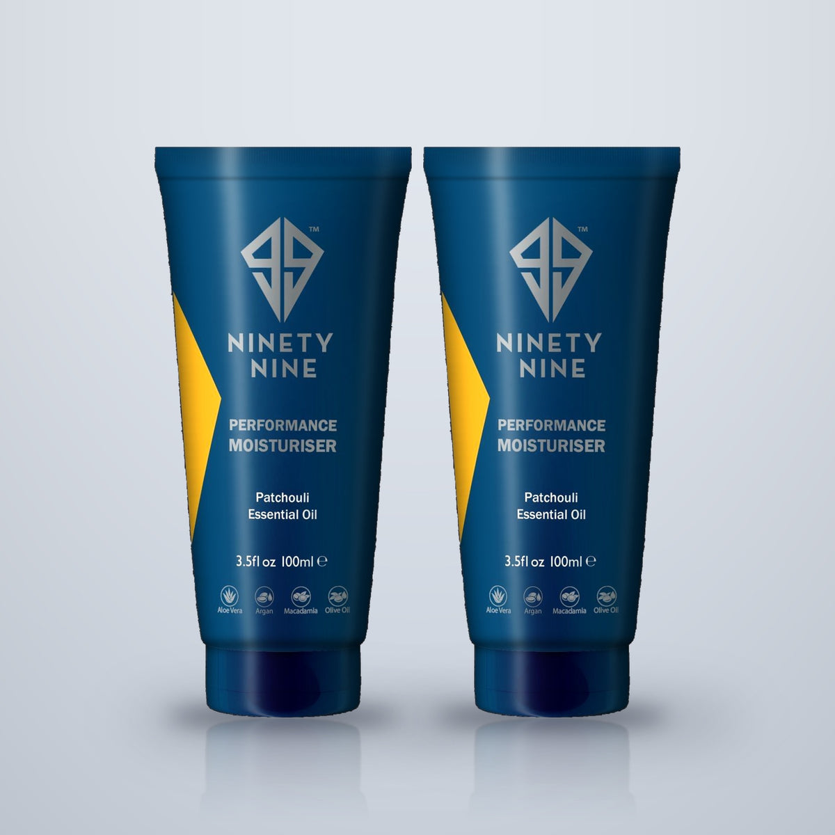 Two blue tubes of Ninety Nine Performance Moisturiser with Patchouli Essential Oil, displayed side-by-side on a light gray reflective surface.