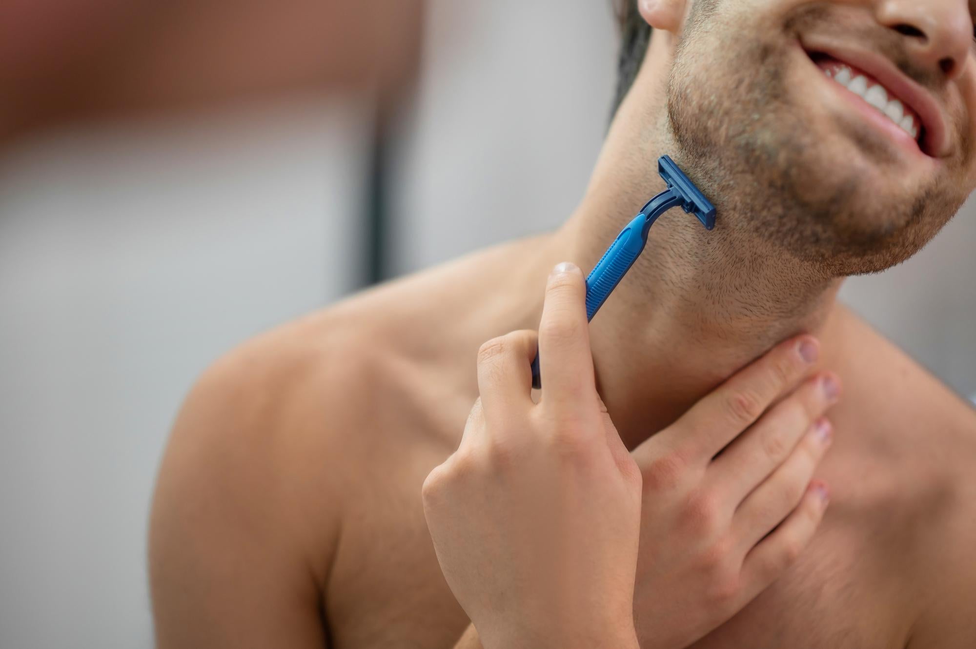 Man shaving his neck with a blue razor, blurred background
